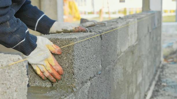 Worker wearing gloves aligning concrete blocks with a string during professional concrete wall installation in Pearson, GA.