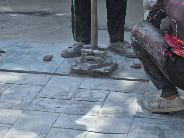 A man skillfully uses a hammer to shape and level a concrete floor during construction work, showcasing stamped concrete services in Paybestain GA.