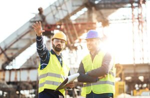 Best concrete contractors in Dallas, GA—two men in hard hats and vests discussing plans and surveying a construction site.