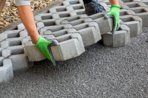 A man carefully places concrete blocks on a sidewalk, demonstrating construction work in progress for driveway installation in Pearson, GA.