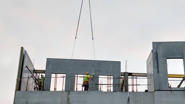 Workers on a building's roof, engaged in concrete wall installation, with a crane positioned nearby.