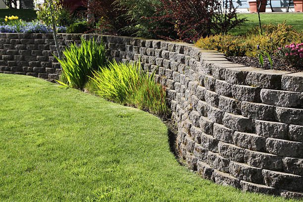 A grassy area featuring a stone retaining wall and a bright red fire hydrant positioned nearby.