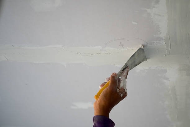 A person using a knife to slice through a piece of white plaster, illustrating drywall repair Near Me