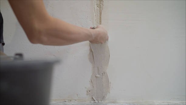 A person actively using a tool to strip plaster from a wall, illustrating a Drywall Repair Near Me
