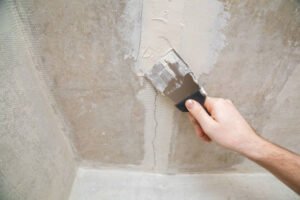 A person using a tool to scrape plaster off a wall, demonstrating drywall repair techniques.