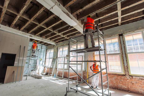 A man repairs a chipped concrete surface while working on a scaffold inside a building.