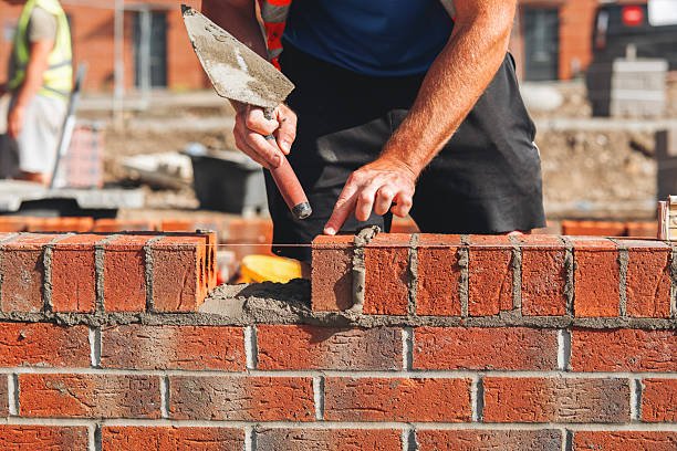 A man repairs a brick wall, focusing on fixing a chipped concrete surface. concrete contractors in Atlanta