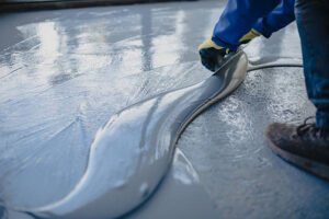 A person painting a floor with a roller, focusing on repairing a chipped concrete surface.