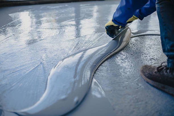 A person painting a floor with a roller, focusing on repairing a chipped concrete surface. concrete contractor tips