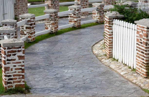 A scenic stone pathway with white picket fencing and a brick wall, highlighting a charming landscape design.