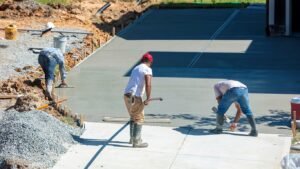 A group of men experienced in constructing commercia walkways pouring concrete to construct a commercial driveway, focused on creating a smooth surface. 