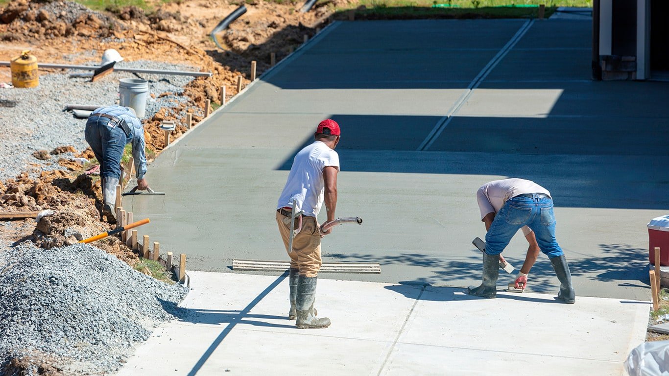 A group of men experienced in constructing commercia walkways pouring concrete to construct a commercial driveway, focused on creating a smooth surface.